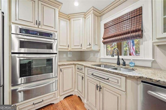 kitchen with light stone countertops, cream cabinets, stainless steel appliances, and sink