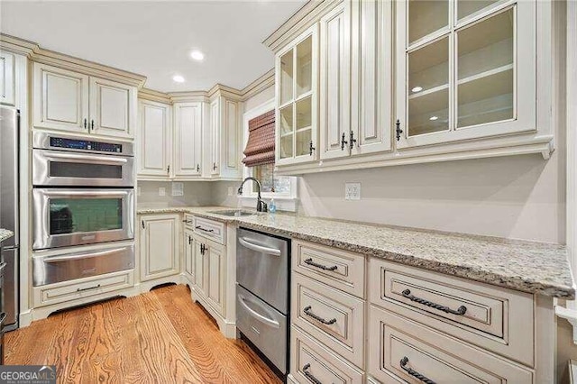 kitchen with light stone countertops, sink, double oven, cream cabinets, and light wood-type flooring