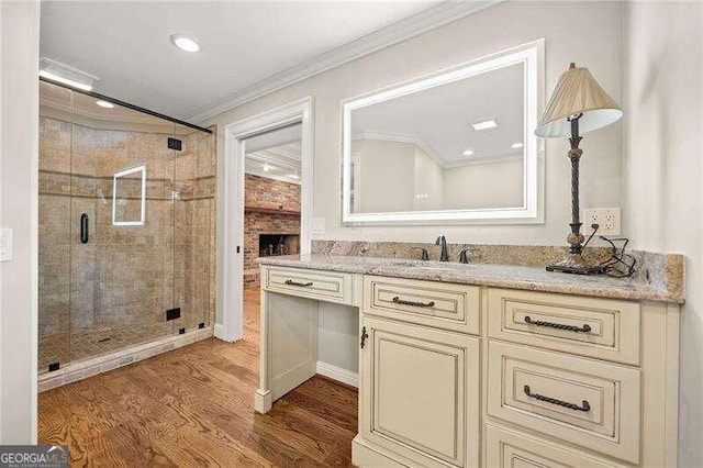 bathroom featuring vanity, crown molding, hardwood / wood-style flooring, a fireplace, and a shower with shower door