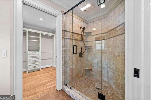 bathroom with hardwood / wood-style floors, a shower with shower door, and crown molding