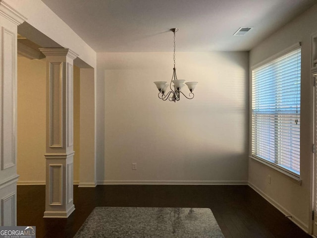 unfurnished dining area featuring a chandelier, decorative columns, and dark wood-type flooring