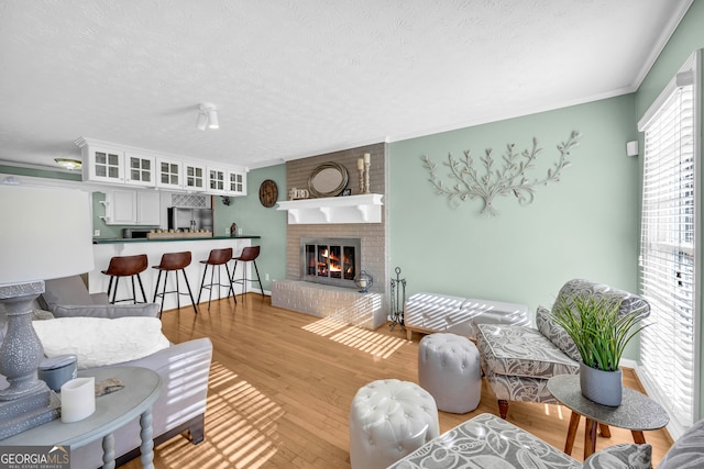 living room with light hardwood / wood-style floors, ornamental molding, a textured ceiling, and a brick fireplace