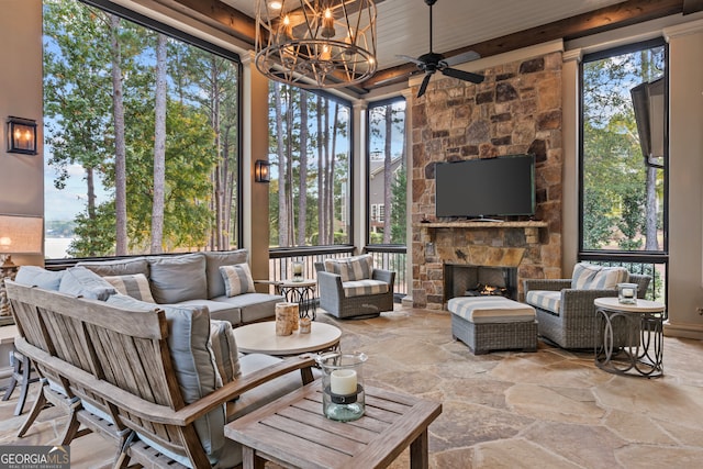 sunroom / solarium with beamed ceiling, an outdoor stone fireplace, and ceiling fan with notable chandelier