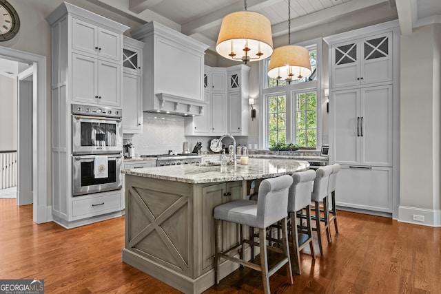 kitchen featuring pendant lighting, a kitchen island with sink, sink, beamed ceiling, and stainless steel appliances