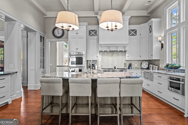 kitchen featuring beam ceiling, a kitchen island with sink, and dark wood-type flooring