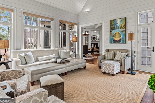 living room featuring a chandelier, wood-type flooring, high vaulted ceiling, and wooden walls