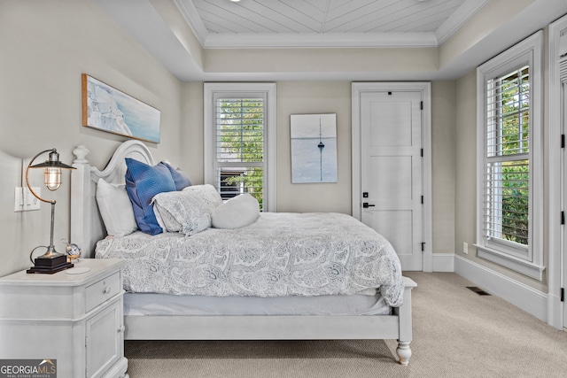 bedroom featuring ornamental molding, light carpet, a tray ceiling, and multiple windows