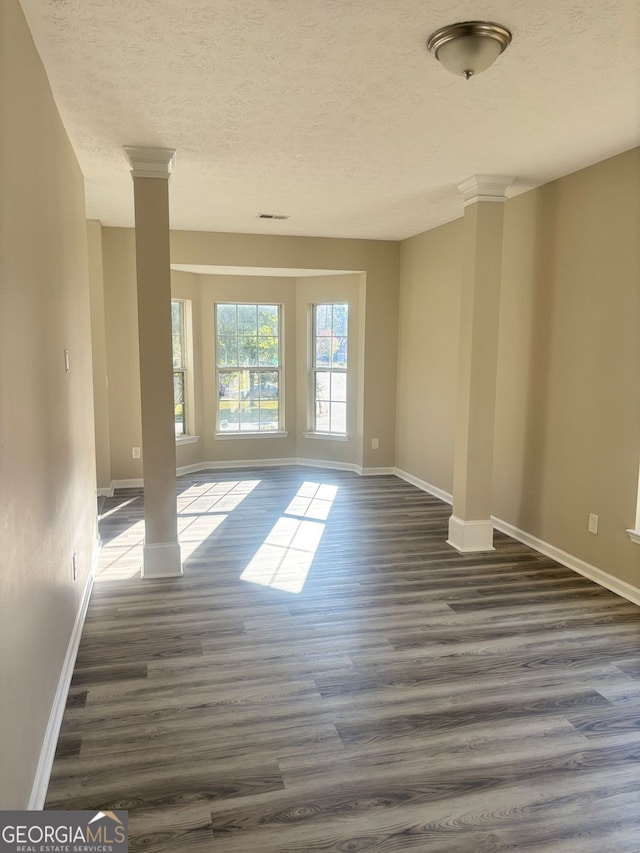 spare room with a textured ceiling, dark hardwood / wood-style floors, and ornate columns