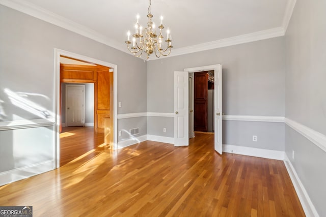 unfurnished room with ornamental molding, a notable chandelier, and hardwood / wood-style flooring