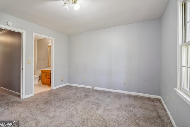 unfurnished bedroom featuring ensuite bath and light colored carpet