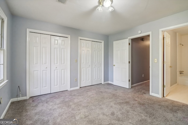 unfurnished bedroom with light carpet, two closets, and ensuite bath