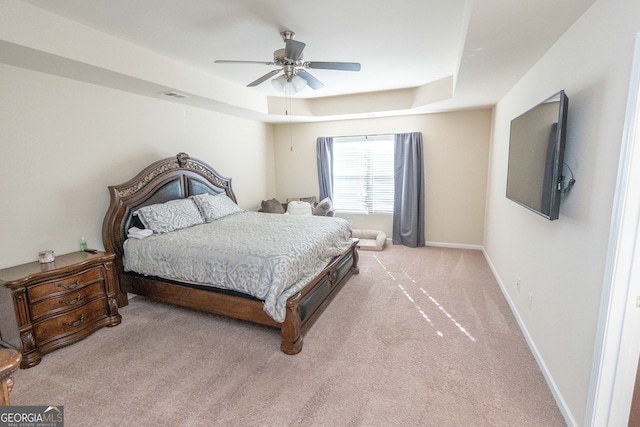 carpeted bedroom with a raised ceiling and ceiling fan