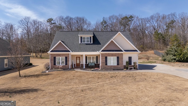 craftsman-style house with brick siding, covered porch, concrete driveway, and a front yard