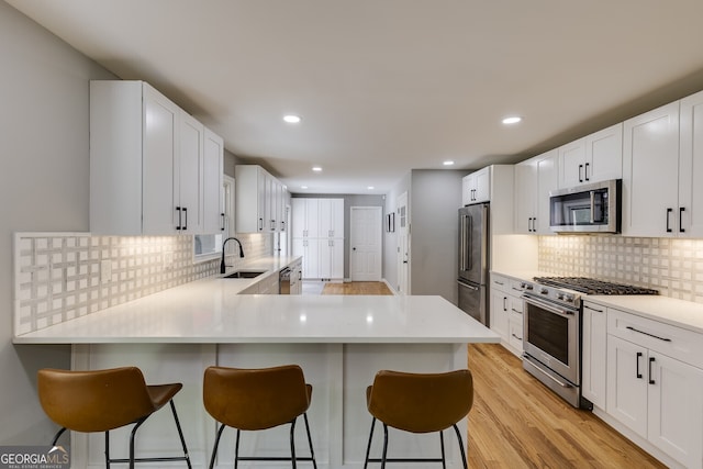 kitchen featuring kitchen peninsula, light hardwood / wood-style floors, a kitchen bar, white cabinets, and appliances with stainless steel finishes