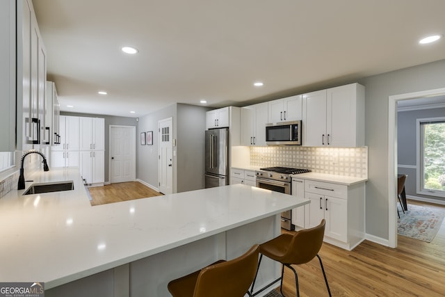 kitchen featuring a kitchen breakfast bar, kitchen peninsula, appliances with stainless steel finishes, light hardwood / wood-style floors, and white cabinetry