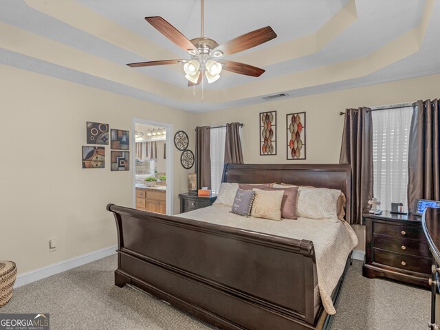 bedroom featuring a raised ceiling, ensuite bath, and ceiling fan