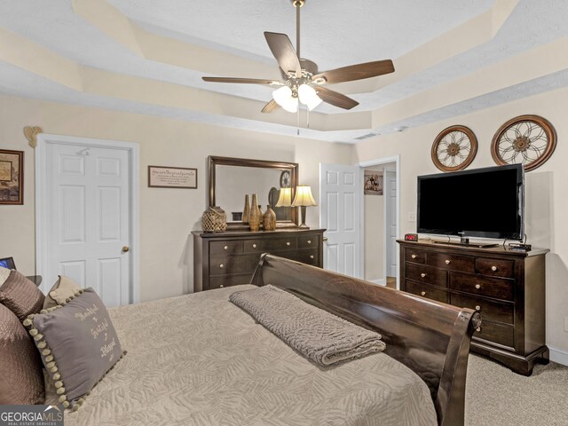 carpeted bedroom featuring ceiling fan and a tray ceiling