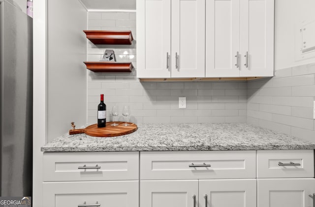 kitchen with white cabinets, stainless steel fridge, light stone countertops, and backsplash