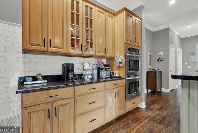 kitchen with dark wood-type flooring, double oven, dark stone countertops, crown molding, and decorative backsplash