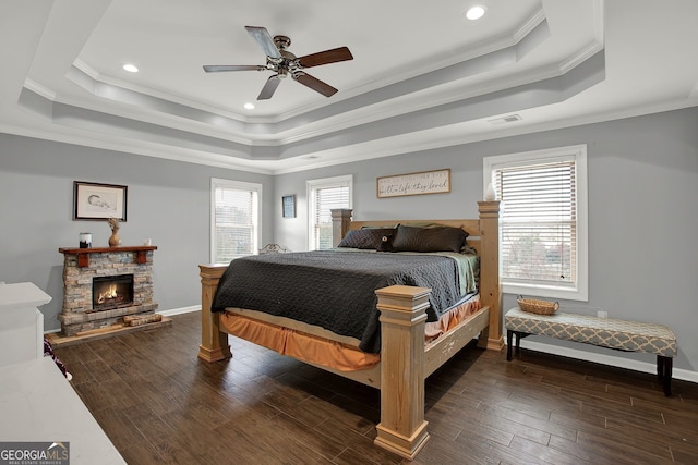 bedroom with dark hardwood / wood-style floors, ceiling fan, ornamental molding, a fireplace, and a tray ceiling