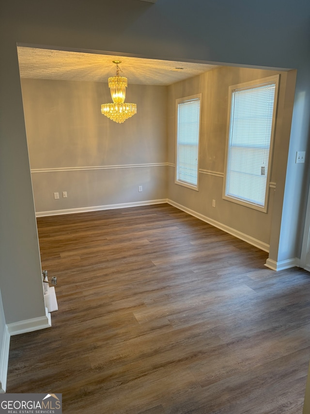 unfurnished dining area featuring dark wood-type flooring, a textured ceiling, and an inviting chandelier