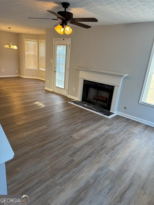 unfurnished living room featuring ceiling fan with notable chandelier, a textured ceiling, and dark hardwood / wood-style flooring