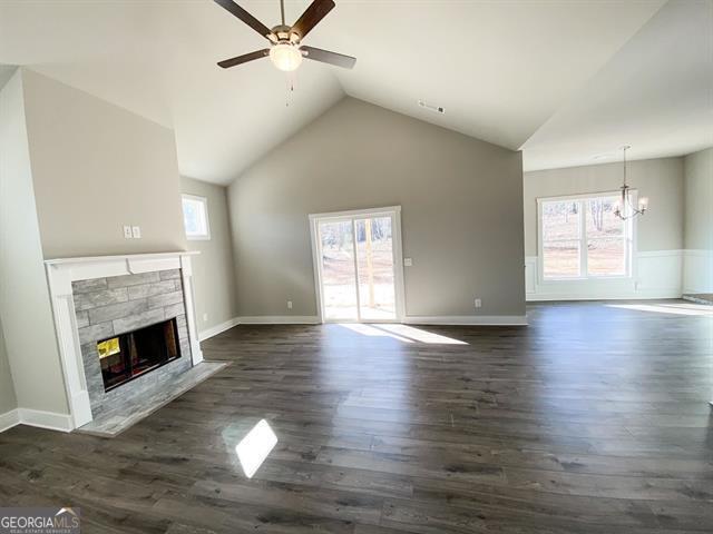 unfurnished living room featuring ceiling fan with notable chandelier, high vaulted ceiling, dark hardwood / wood-style floors, and a stone fireplace