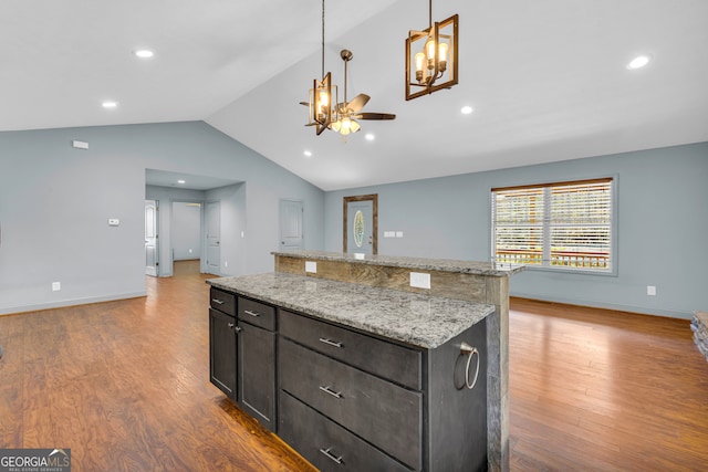 kitchen featuring pendant lighting, lofted ceiling, light wood-type flooring, light stone counters, and dark brown cabinetry