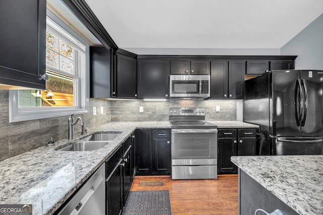 kitchen with light stone countertops, sink, stainless steel appliances, tasteful backsplash, and light hardwood / wood-style flooring