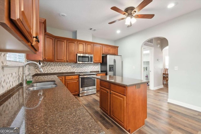 kitchen featuring dark stone counters, stainless steel appliances, sink, a center island, and dark hardwood / wood-style floors