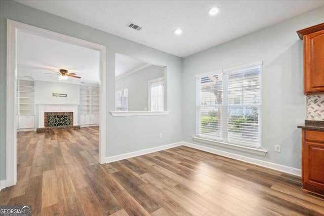 interior space with dark hardwood / wood-style floors, ceiling fan, ornamental molding, a fireplace, and built in features