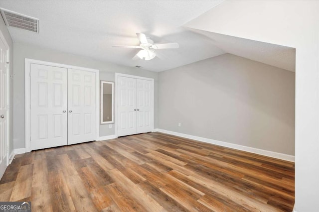 unfurnished bedroom featuring vaulted ceiling, hardwood / wood-style flooring, ceiling fan, a textured ceiling, and multiple closets