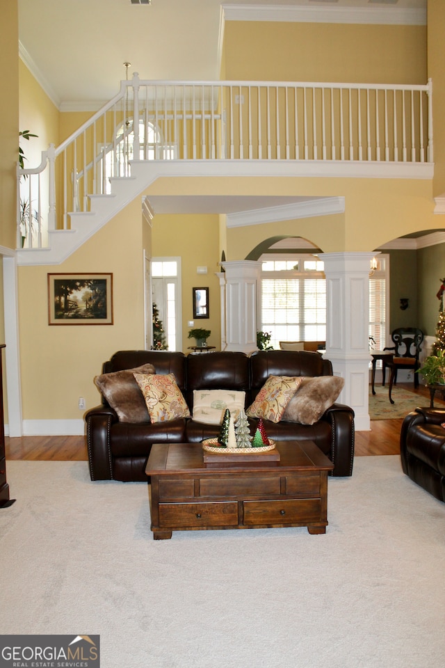 living room featuring wood-type flooring, crown molding, a towering ceiling, and decorative columns