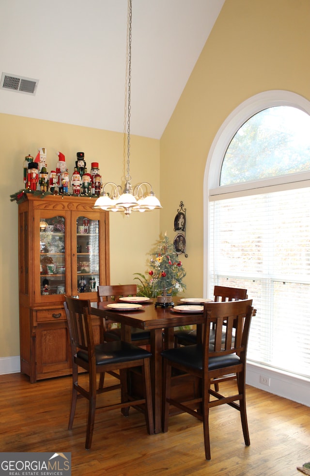 dining area with an inviting chandelier, high vaulted ceiling, and hardwood / wood-style flooring