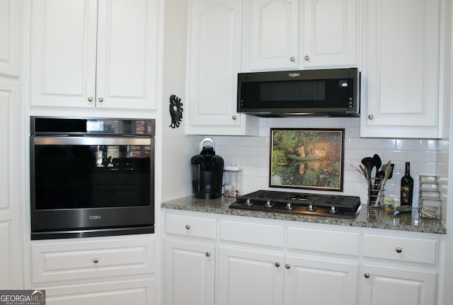 kitchen with backsplash, dark stone countertops, white cabinets, and black appliances