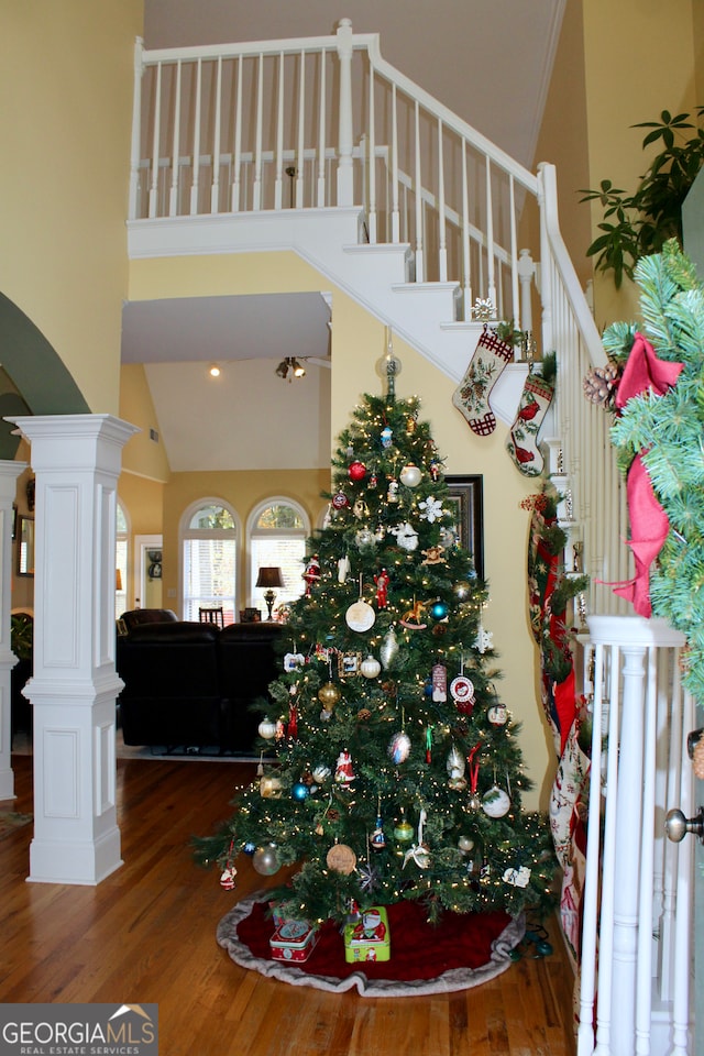 stairway featuring wood-type flooring, high vaulted ceiling, and decorative columns