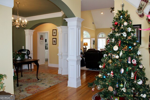 entrance foyer with decorative columns, vaulted ceiling, wood-type flooring, and a chandelier