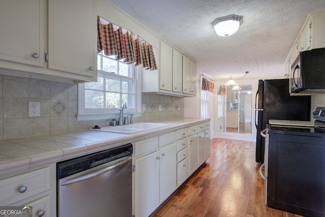 kitchen with range with electric cooktop, tile countertops, stainless steel dishwasher, and white cabinetry