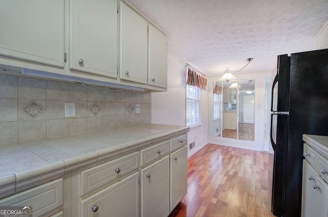 kitchen with tile countertops, white cabinets, black refrigerator, a textured ceiling, and light hardwood / wood-style floors