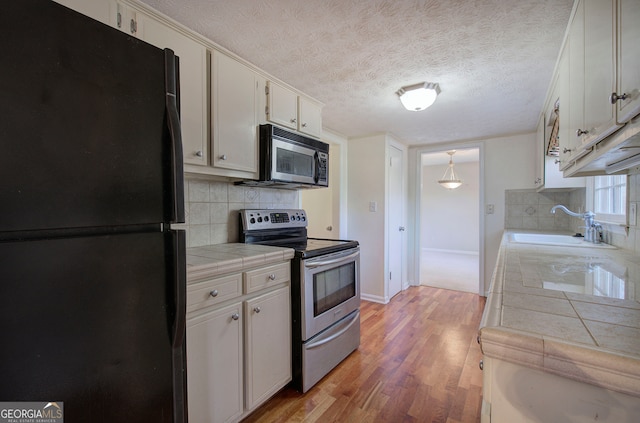 kitchen featuring white cabinetry, sink, backsplash, tile countertops, and appliances with stainless steel finishes