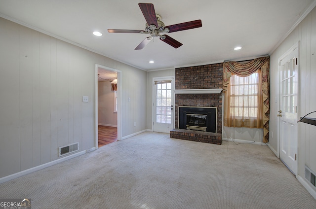 unfurnished living room featuring ceiling fan, crown molding, light carpet, and a brick fireplace