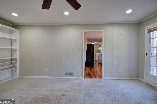 carpeted spare room with ceiling fan, wooden walls, and ornamental molding