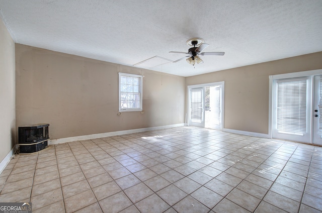 tiled empty room featuring ceiling fan, a wood stove, a textured ceiling, and french doors