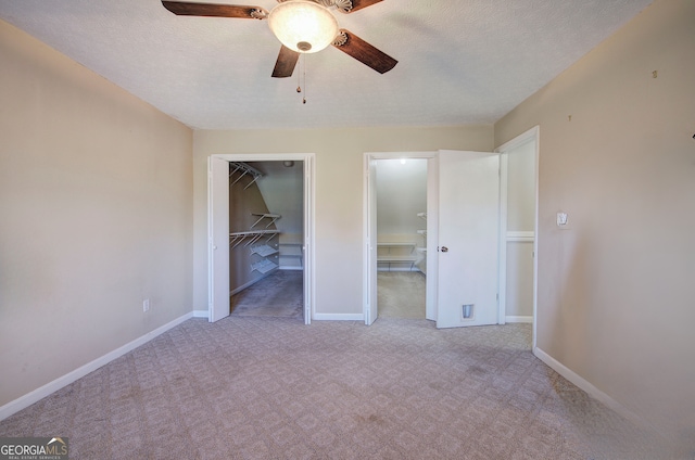 unfurnished bedroom with ceiling fan, a spacious closet, a textured ceiling, light colored carpet, and a closet