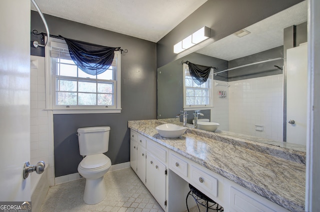 bathroom with vanity, tile patterned flooring, toilet, tiled shower, and a textured ceiling