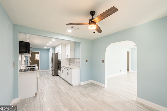 kitchen featuring decorative backsplash, white cabinets, black appliances, and ceiling fan