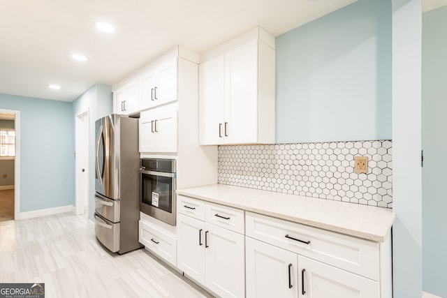 kitchen featuring white cabinets, decorative backsplash, light stone counters, and appliances with stainless steel finishes