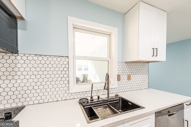 kitchen featuring backsplash, light stone counters, stainless steel dishwasher, sink, and white cabinetry