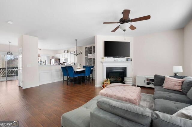 living room with ceiling fan with notable chandelier and dark hardwood / wood-style flooring