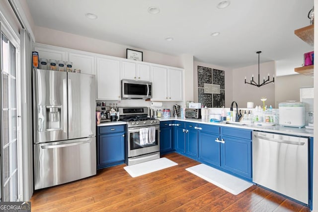 kitchen with pendant lighting, hardwood / wood-style floors, an inviting chandelier, blue cabinetry, and appliances with stainless steel finishes